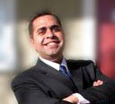 Joe Badin wearing a suit and smiling, background is bright and blurry