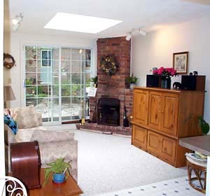 bright living room with skylight, louvered glass doors, corner fireplace, and obsolete furniture. Opens on to kitchen