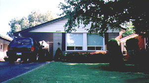 ground level photo of a ranch-style house, drive way on the left houses an SUV, trees on the right
